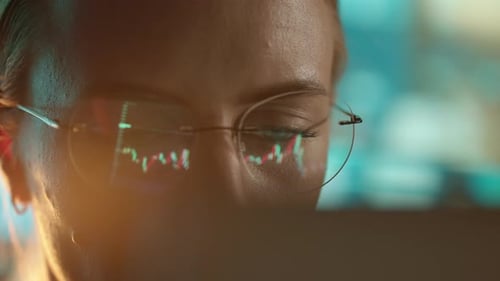 Trader Wearing Glasses is Working on Laptop Computer Screen with Stock Market Charts and Bitcoin BTC