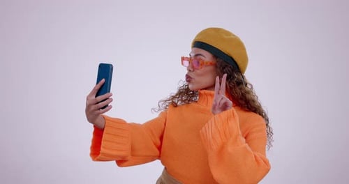 Young woman, studio selfie and peace sign with kiss, smile or tongue out by white background