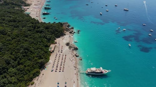 A sandy beach with boats in clear turquoise waters and lush green surroundings, aerial view