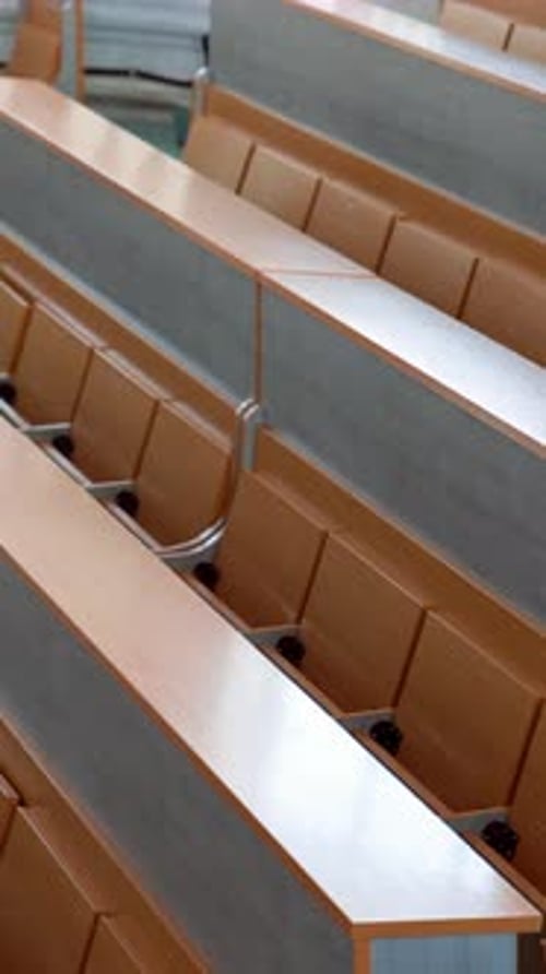 Modern desks in lecture hall. Rows of long wooden tables with vacant seats in the light auditorium