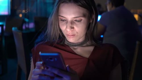 Young woman texting on smartphone at rooftop bar in the city at night