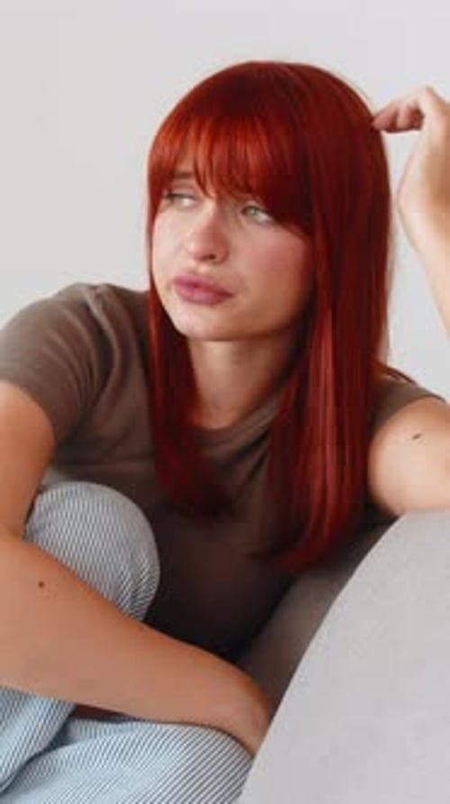 Sad woman with red hair sitting on couch