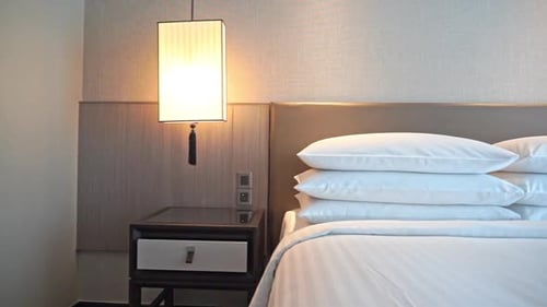 NIght lamp and made-up bed with white striped linen pillows and cover in a hotel resort in Bangkok,