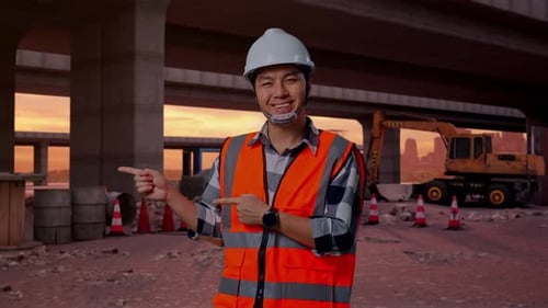 Asian Male Engineer Smiling And Pointing To Side At Building Site
