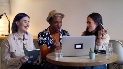 Gruppe junger Freunde oder Kollegen mit Laptop im Café, die Begeisterung zeigen.