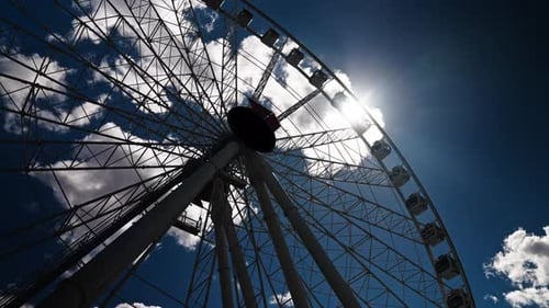 A Lowangle Shot of an Urban Ferris Wheel with Passenger Cabins Silhouetted Against Bright Sunlight