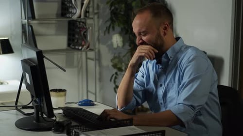 Very tired, bearded male office worker types, yawns