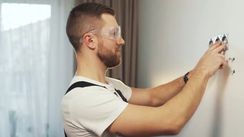 A handsome man in a work uniform installs electrical outlets