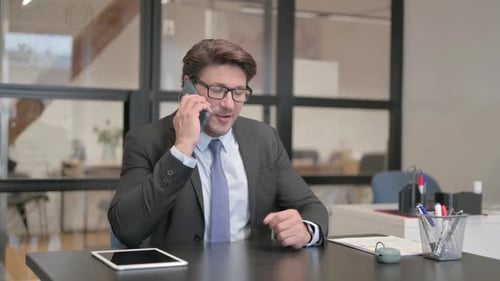 Middle Aged Businessman Talking on phone while Sitting in Office