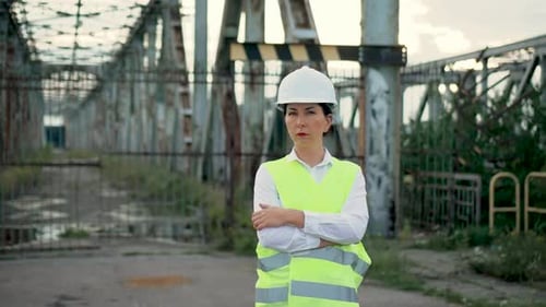Woman Engineer Builder in Protective Vest and Helmet Inspect Standing Crossing Hands Near Metal