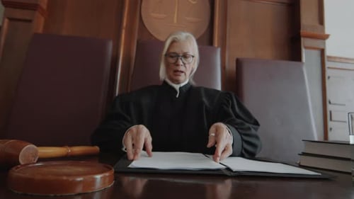 Mature Judge Hitting Sound Block with Gavel and Putting on Glasses