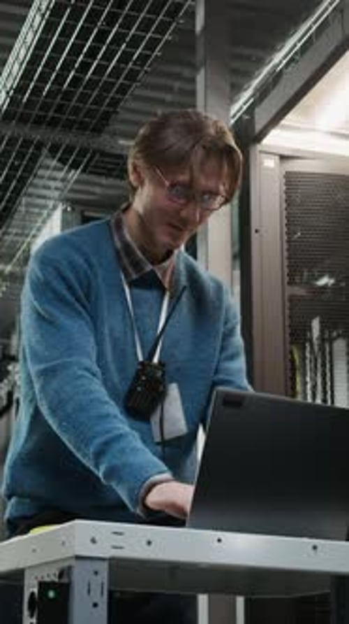 Vertical of Data Center Technician Communicating on Walkie Talkie with Laptop