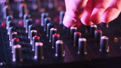 Male Hand Adjusting Buttons on Audio Mixer in Neon Light CloseUp
