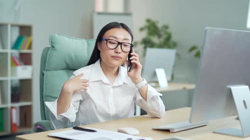 portrait a young asian business woman worker talking on mobile phone in office sitting at desk