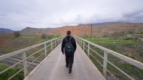 Man Walking on Bridge in Rural Mountain Landscape