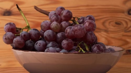 Red grapes rotate on a wooden background.