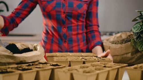 Woman Gardener Adding Black Soil to Vegetable Seeding Trays Close Up Using Small Shovel From Eco