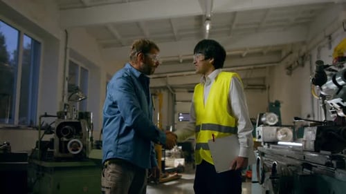 Japanese Engineer Shaking Hands with Mature Wroker Indoors in Metal Workshop