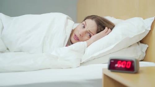 Close up portrait of sleeping woman in bed at home wakes up from the loud sound of the alarm clock