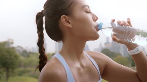 Young fitness woman in sportswear drinking water in city park