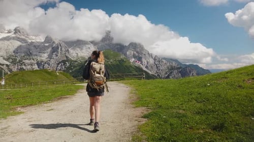 view from behind of a hiker tourist traveler woman with backpack trekking and walking on a mountain
