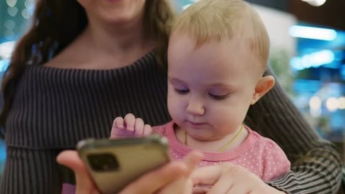 Cute Baby Using Phone While Held by Woman
