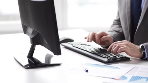 Man Types at Computer, Reviews Charts in Office