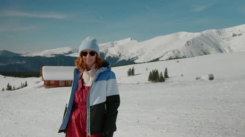 Portrait of woman in panoramic mountain environment with small chalet in the back.