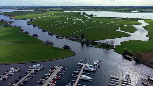 Vista aérea de drone sobre uma marina movimentada com barcos atracados, abrindo-se para um vasto pôlder holandês