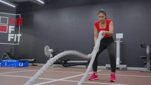 Young asian woman in sportswear doing exercise with rope in the fitness gym sport club.