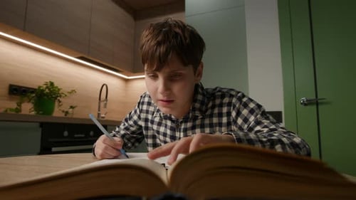 Boy Studying Textbook at Kitchen Table