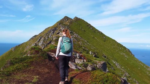 A young brunette woman is walking with her hiking boots and backpack on a trail leading up to the to