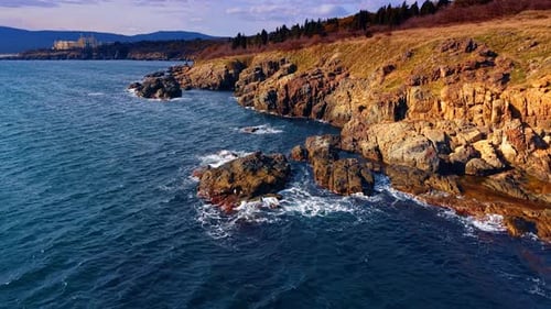 Waves crash against a rocky shoreline with clear blue water. In the background