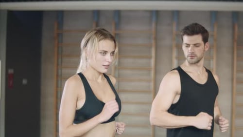 Happy young couple running on treadmill machines together in fitness gym