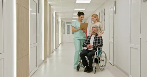 MiddleAged Man in Wheelchair at Hospital with Nurse and Companion