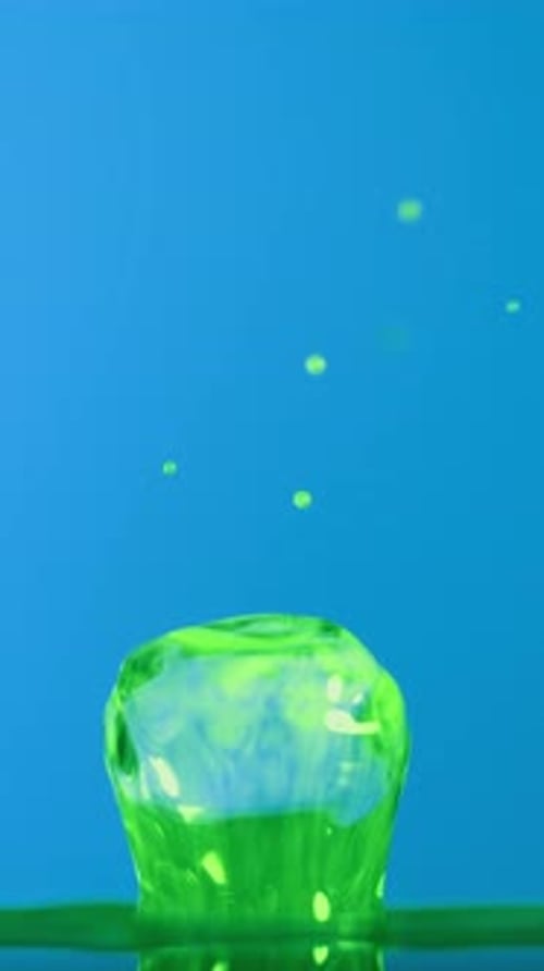 Dynamic Green Water Droplet Impacting Splash Against Blue Background