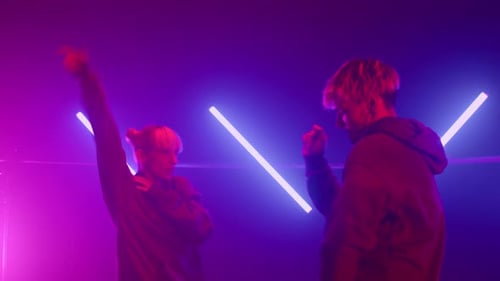 Trendy blond couple dancing hip hop battle on night club stage in ultraviolet lights
