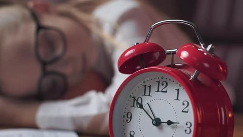 Peaceful Child Sleeping at Desk with Red Alarm Clock Indoors