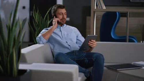 Confident businessman in modern office working with laptop and talking on cell phone
