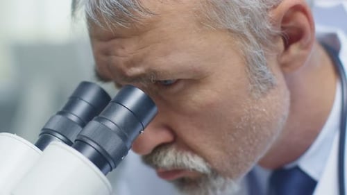 Close-up of a Senior Male Doctor Conducting Health Issue Research Through Microscope.