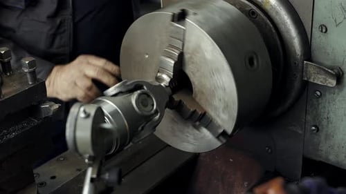 An elderly turner works at a lathe processes the metal part on a lathe in a lathe shop