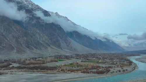 Aerial scenic view of a vast mountain valley with a river flowing through and low clouds touching th