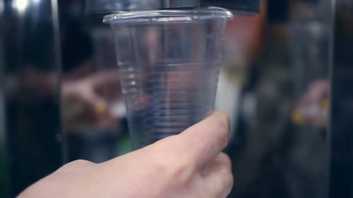 Hand holding plastic cup as mineral water flows and overflows in refreshing splash