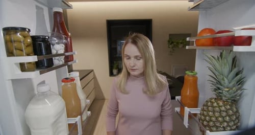 Attractive Middle Aged Woman Takes Containers of Food From the Refrigerator View From Inside the