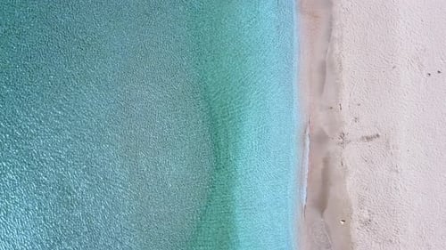 Top-down aerial view of an empty tropical white sands beach and water as it ripples gently in the su