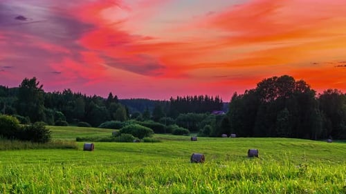 Beautiful grassfields with straw bales lying under colorful sky with cirrus clouds in motion from da