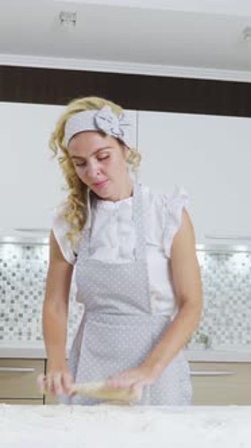 Woman in Gray Apron Rolling Dough on Kitchen Counter with Flour and Utensils Around