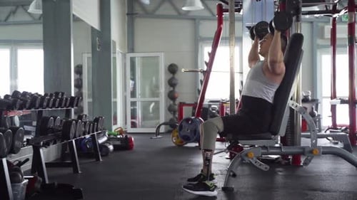 Disabled man with prosthetic leg lifting dumbbells in the gym during workout