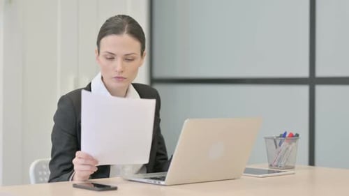 Woman Reviews Documents at Desk with Laptop
