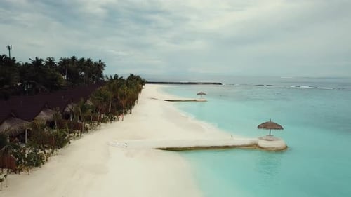 Vídeo de drone de um resort tropical nas Maldivas, lagoa azul, palmeiras verdes, águas rasas turquesas,
